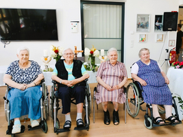 Vier ältere Frauen in Rollstühlen sitzen in einem Raum mit Blumen und Dekorationen.