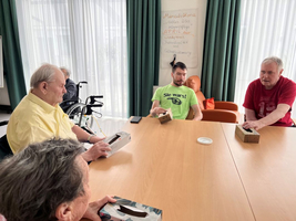 Vier Personen sitzen an einem Tisch und halten jeweils eine Box in der Hand.