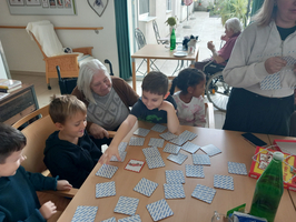 Kinder und Erwachsene spielen gemeinsam mit Karten in einem hellen Raum.