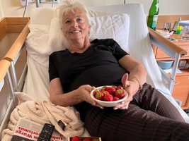 Eine ältere Frau im Bett hält eine Schüssel mit frischen Erdbeeren.