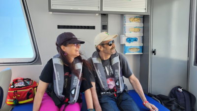 Ein Paar sitzt in einer Kabine in einem Boot. Beide tragen Rettungswesten. Sie schauen in die Ferne und lächeln.