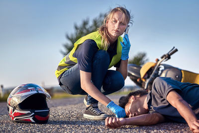 Eine Rettungskraft kümmert sich um einen verletzten Motorradfahrer am Straßenrand.
