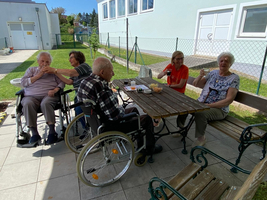 Ältere Menschen sitzen draußen an einem Tisch und genießen snacks und Getränke.