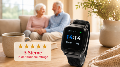 Auf dem Tisch liegt eine Smartwatch mit schwarzem Armband, die die Uhrzeit anzeigt. Im Hintergrund sitzen ein älteres Paar auf einer Couch und lächeln sich an. Links daneben steht eine Tasse. Ein Textfeld zeigt 