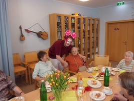 Eine Gruppe älterer Menschen feiert mit einem clownartigen Animateur in einem Gemeinschaftsraum.
