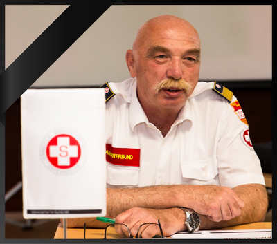 Ein Mann in Uniform spricht an einem Tisch mit einem Flaggenbanner im Hintergrund.