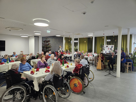 Weihnachtsfeier mit Senioren in einem geschmückten Raum, Musikdarbietung auf der Bühne.