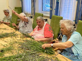 Ältere Frauen arrangieren Lavendelzweige an einem Tisch in einem Gemeinschaftsraum.