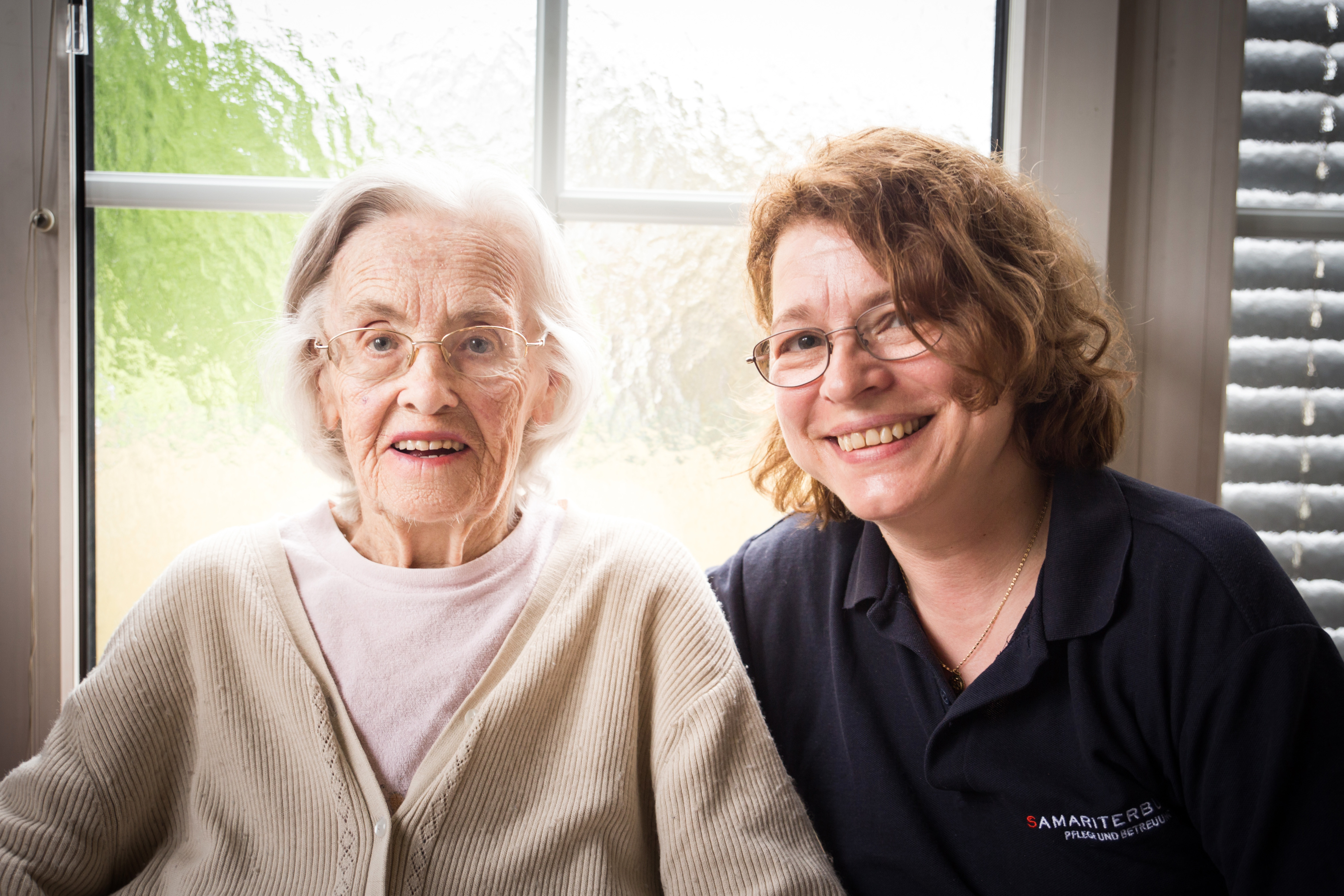 Ältere Dame und ihre Heimhilfe lächeln in Kamera