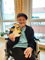 Eine ältere Frau sitzt im Rollstuhl und hält eine Papierfigur eines Engels.