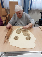 Eine ältere Frau rollt Teig mit einer Nudelrolle und formt ihn.