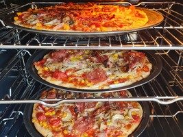 Drei Pizzen in einem Ofen, frisch gebacken auf verschiedenen Backblechen.