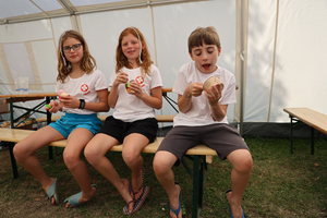 Drei Kinder sitzen in einem Zelt und genießen Eiscreme.