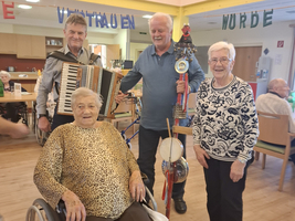 Vier Personen, darunter eine Frau im Rollstuhl, mit Musikinstrumenten in einem Raum.