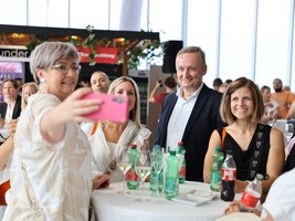 Eine Gruppe von Menschen posiert beim Selfie an einem Tisch mit Getränken.