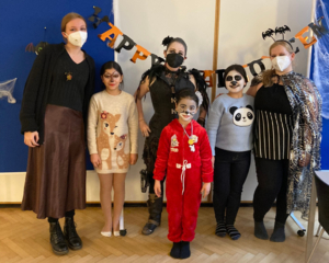 Gruppenfoto kostümierte Kinder im LernLEO mit Betreuerinnen, im Hintergrund Happy Halloween Girlande