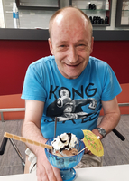 Lächelnder Mann mit einer großen Schüssel Eis und buntem Schirmchen.