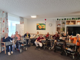 Ältere Menschen sitzen in einem Raum und halten Musikinstrumente in den Händen.