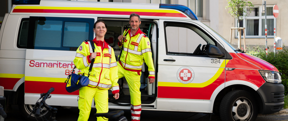 Mitarbeiter:innen im Rettungsdienst vor Rettungsauto