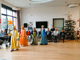 Sternsinger in festlicher Kleidung präsentieren sich vor Senioren und einem Weihnachtsbaum.