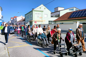 Eine Gruppe von Menschen, darunter Ältere, marschiert auf einer Straße.