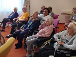 Ältere Menschen in Rollstühlen während einer Veranstaltung in einem Gemeinschaftsraum.