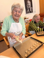 Eine ältere Frau backt Plätzchen und lächelt in einer freundlichen Umgebung.