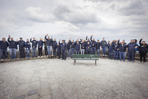 Gruppe von Personen winkt fröhlich vor einer Bank im Freien.