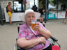 Ältere Frau in einem Rollstuhl hält ein Getränk in der Hand.