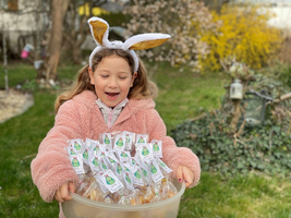 Ein Mädchen mit Hasenohren hält einen Behälter voller Ostergeschenke.