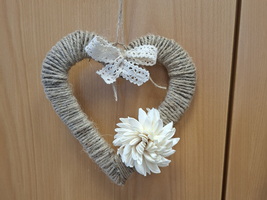 Ein herzförmiger Kranz aus Jute mit einer weißen Blume und einer Schleife.