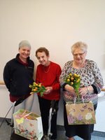 Drei Frauen lächeln und halten Blumensträuße in einer Einrichtung.