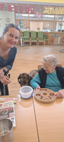 Eine Betreuerin interagiert mit einem Hund vor einer Gruppe älterer Menschen.