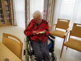 Eine ältere Frau im Rollstuhl hält ein Lebensmittel in der Hand.