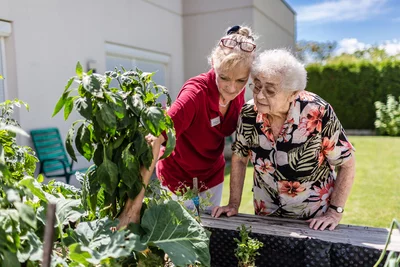 Eine Frau zeigt einer älteren Dame Pflanzen in einem Garten.