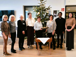 Eine Gruppe von neun Personen steht lächelnd vor einem Weihnachtsbaum.