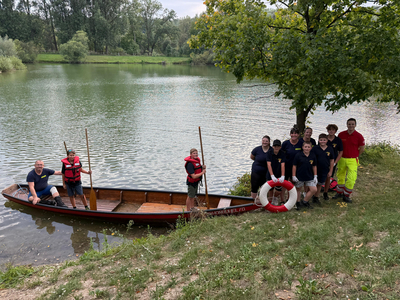Eine Zille im Wasser in der drei Feuerwehrleute sind. Daneben eine Gruppe von Jugendkinder und einem Sanitäter