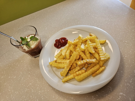 Ein Teller mit Pommes frites und Ketchup, daneben ein Glas Dessert.