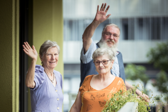 3 Bewohner:innen einer Senioren-WG winken fröhlich