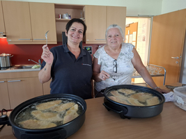 Zwei Frauen stehen an einer Kochstelle und frittieren Fisch.