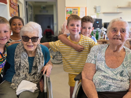 Eine ältere Frau in einem Rollstuhl umgeben von lachenden Kindern.