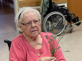 Eine ältere Frau in einem Rollstuhl hält Lavendelblüten in der Hand.