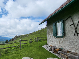 Eine malerische Berglandschaft mit einem kleinen Haus und grünen Wiesen.