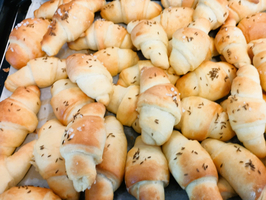 Ein Tablett mit frischen, goldbraunen Croissants, die leicht knusprig sind. Einige sind mit Kümmel oder grobem Salz bestreut. Die Croissants sind gleichmäßig geformt und dicht nebeneinander angeordnet.
