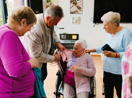 Ältere Frauen helfen einer Seniorin im Rollstuhl, sich umzuziehen.