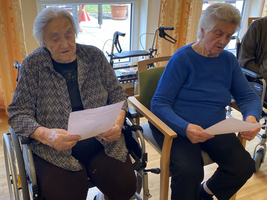 Zwei ältere Frauen sitzen in Stühlen und lesen Dokumente.