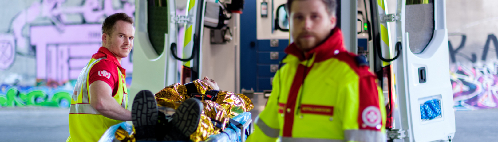 Zwei Samariterbund-Sanitäter mit Patienten auf der Krankentrage vor einem Rettungswagen