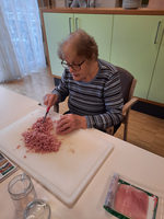 Eine ältere Frau schneidet Fleisch auf einem Schneidebrett in kleine Stücke.