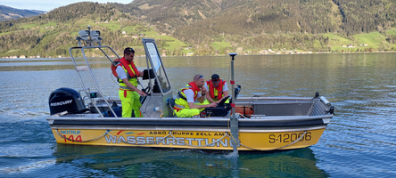 Rettungsboot mit Helfern auf einem Gewässer in Berglandschaft unterwegs.