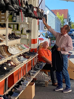 Zwei Männer in einem Schuhgeschäft, einer betrachtet Stiefel, während der andere sitzt.